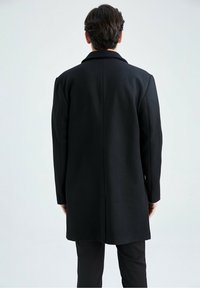 Schwarzer Wollmantel mit klassischem Kragen, geradem Schnitt, langen Ärmeln und Seitentaschen; glatte Textur und maßgeschneidertes Design.