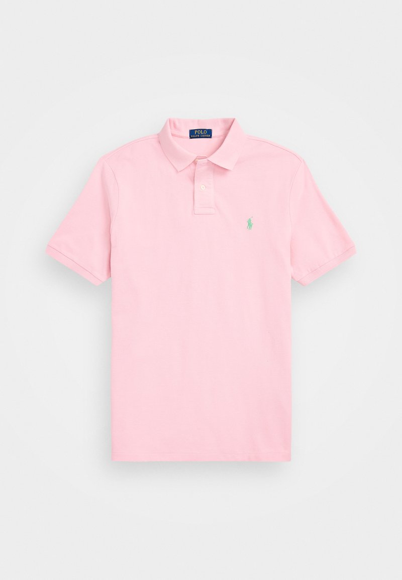 Ljusrosa polo-shirt i bomull. Har en klassisk krage, korta ärmar och en liten grön logotyp på vänster bröst.
