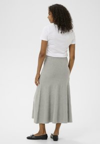 Jupe en tricot gris à forme évasée, dotée d'une taille flexible. Associée à un t-shirt blanc et des ballerines noires, vue de dos.