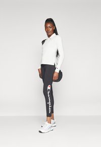 Outfit sportivo composto da una maglia a maniche lunghe bianca con accenti neri, leggings neri con logo "Champion" bianco e scarpe da ginnastica bianche.