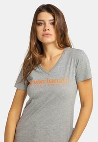 Grå V-hals t-shirt med korta ärmar som har fet orange text. Tyget ser slätt ut med en avslappnad passform. Enkelt mönster, inga mönster.