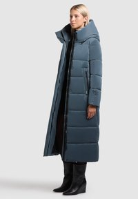 Hele sinine pikk puffer-jakk kõrge kraega, tikandite tekstuuriga, küljetaskudega ja lukuga. Kanna koos mustade põlvekõrguste platvormkingadega.