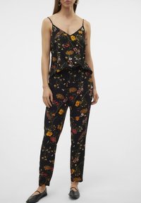 Ensemble deux pièces noir à fleurs composé d'un débardeur imprimé à fines bretelles et d'un pantalon ample, tous deux ornés de motifs floraux colorés.