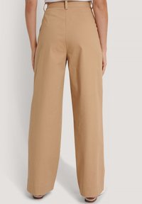 Beżowe spodnie szerokie z gładkim, teksturowanym wykończeniem i średnim stanem, z prostym designem pętelek na pasek i bez widocznych kieszeni.