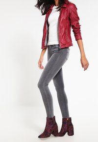 Giubbotto in pelle rossa da motociclista sopra un top in maglia bianca, abbinato a jeans grigi e stivaletti con stampa floreale viola e tacco a blocco.