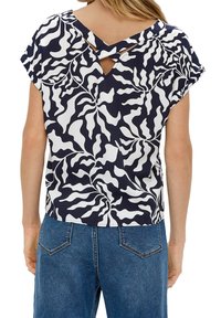 Haut à motifs bleu marine et blanc avec une finition texturée, doté de manches courtes et d'un détail croisé dans le dos. Porté avec un jean bleu.