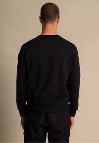 Sudadera negra con mangas largas, escote redondo y puños y dobladillo acanalados. La tela parece suave con detalles mínimos de costuras.