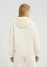 Crème-kleurige hoodie met een zachte, gladde textuur, oversized ontwerp, verlaagde schouders en een dubbellaagse capuchon, die op de taille zit.