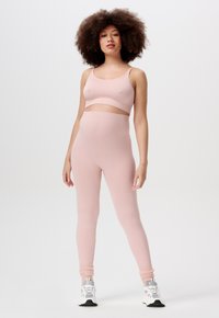 Ensemble de sport à côtes rose clair comprenant un débardeur court et un legging taille haute. La texture du tissu est lisse, avec des détails de design ajustés.