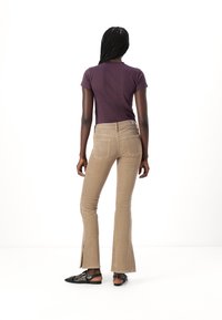 Brown flared pants with a textured fabric, featuring two back pockets and a side slit at the hem. Paired with a fitted purple shirt.