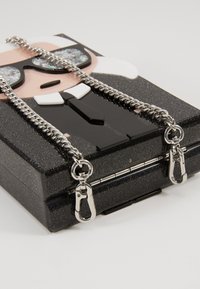 Black glitter clutch with silver chain straps. Features a pop art design of a character in sunglasses, smooth surface, and metallic accents.