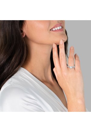 Sterling-Silberring mit einem zentralen klaren Stein, eingefasst in ein gedrehtes Banddesign. Die Hand des Models ist in der Nähe des Gesichts positioniert und trägt ein weißes Oberteil.