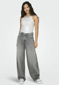 Grå, vide bukser med høj talje og bindebånd foran, parret med en tætsiddende hvid tanktop og hvide sneakers. Glat tekstur.