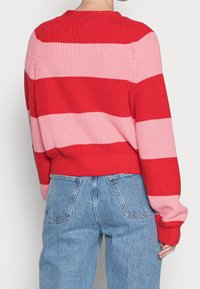 Röd och rosa randig stickad tröja med vid halsringning och ribbad nederkant; kombinerad med högmidjade blå jeans.