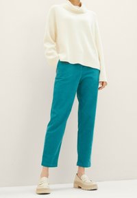 Pull blanc à côtes avec un col bateau, associé à un pantalon en velours côtelé turquoise. Tenue complétée par des mocassins à plateforme beiges.