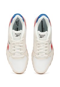 Zapatillas blancas con acentos rojos y azules, suela de goma texturizada, diseño con cordones y marca Reebok en la lengüeta y los laterales.