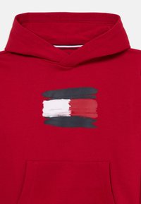 Sweat à capuche rouge en coton avec une poche frontale et un imprimé abstrait audacieux en blanc, noir et rouge au centre.