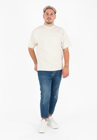 Crème kortef mouwen shirt met een voorkruiszak, gecombineerd met blauwe denim jeans en witte sneakers, met een relaxte pasvorm en een gladde textuur.