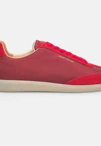 Roter Sneaker mit glattem Obermaterial, das ein Rautenmuster aufweist, Wildlederakzente und eine strukturierte cremefarbene Sohle. Die Schnürsenkel sind in passendem Rot für einen harmonischen Look.