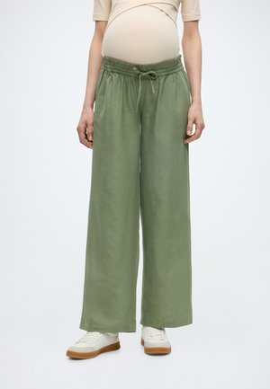 Rase uus beezat topsi, lahtised rohelised nööriga püksid ja valged tossud ühevärvilisel taustal.