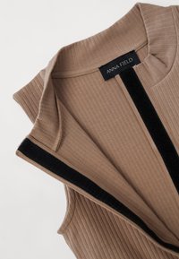 Brown ribbed sleeveless top featuring a collar and black velvet accents along the front. The label reads "ANNA FIELD."
