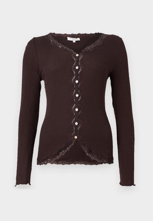Ruskea raidoitettu pitkähihaine cardigan, jossa on pitsireunat ja aaltoilevat reunat. Tässä mallissa on V-pääntie ja seitsemän nappia edessä.