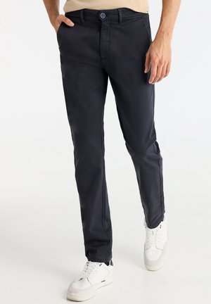 Chinos de color azul marino oscuro, confeccionados en algodón, con un diseño de pierna recta. Cuentan con cierre de botón, pasadores para cinturón y bolsillos, combinados con zapatillas blancas.