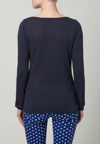 Marinefarbener Langarmoberteil mit weitem Ausschnitt und strukturiertem Stoff, kombiniert mit blauen Polka-Dot-Hosen. Das Design ist einfach und lässig.
