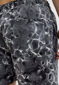 Pantaloni da bagno da uomo con un motivo d'acqua nero e grigio, fascia elastica in vita e tasca posteriore con un accento circolare. Tessuto liscio.