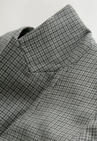 Hall hallruuduline kangas struktureeritud krae disainiga, millel on peen muster väikestest tumedatest ruutudest ja sile tekstuur.