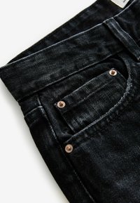 Jeans de mezclilla negra con un diseño ajustado, costuras visibles, un pequeño bolsillo frontal y remaches de cobre en la parte delantera.