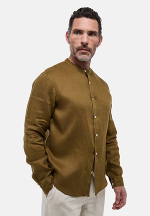 Chemise marron à manches longues avec col fantaisie, dotée d'une ouverture à boutons et d'une texture de tissu lisse. Portée avec un pantalon de couleur claire.