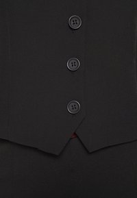 Gros plan sur un gilet noir boutonné avec trois boutons visibles sur un pantalon noir assorti.