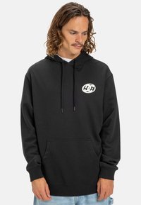 Black hoodie made of cotton with long sleeves, a front pocket, and a white circular logo on the chest. Features drawstring at the hood.