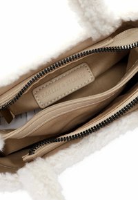 Beige inner lining with a soft, fluffy white trim. Two zippered compartments and an embossed label reading "EMILY & NOAH."