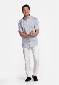 Korte mouwen blouse in lichtblauw met kleine witte patronen, gecombineerd met crèmekleurige broeken en zwarte schoenen.