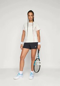 Tennisiv outfit, mis on valmistatud heledast hallist lühikeste varrukatega topist roosa aktsendiga, mustadest lühikestest pükstest ja valgetest spordijalatsitest siniste üksikasjadega. Koos tennise reketiga.