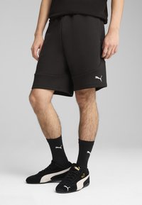 Pantalones cortos deportivos negros con una textura suave, que cuentan con una cintura elástica y bolsillos laterales. Combinados con zapatillas negras y calcetines acanalados.