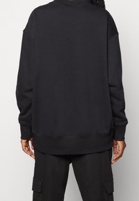 Sudadera negra de gran tamaño con cuello redondo, hombros caídos y puños y dobladillo acanalados, hecha de una tela suave y texturizada.