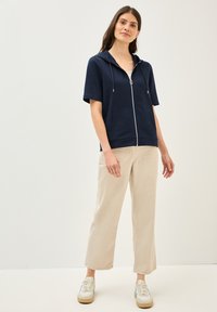 Hoodie zippé à manches courtes en marine, confectionné dans un tissu doux, avec une poche avant. Accompagné d'un pantalon large beige clair et de baskets décontractées.