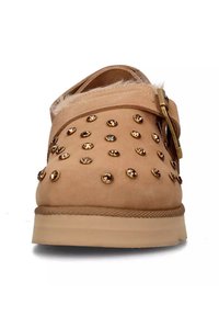 Scarpa slip-on beige in materiale scamosciato, con borchie dorate e suola texturizzata. Include una cinturino decorativo con una fibbia in metallo.