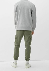 Grijze sweatshirt met geribbelde manchetten, gecombineerd met olijfgroene cargobroek met voorzakken, taps toelopende enkels en witte sneakers.