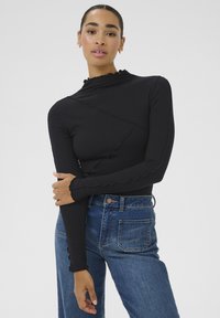 Maglione a maniche lunghe nero a costine con collo alto e bordi arricciati, abbinato a jeans denim blu a vita alta con tasca posteriore.