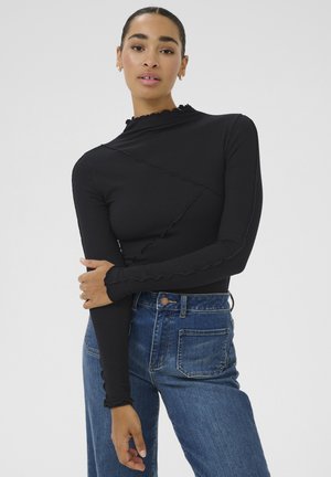 Haut noir à manches longues côtelé avec un col montant et des bords volants, associé à un jean en denim bleu taille haute avec une poche arrière.