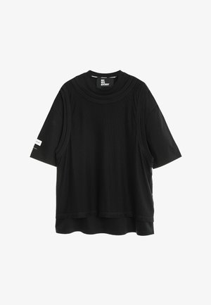 Camiseta negra de manga corta con una superposición sin mangas de malla negra suelta y un pequeño logo blanco en la manga izquierda.