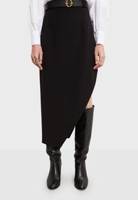 Crna suknja s asimetričnim rubom, izrađena od glatkog materijala, uparen s čizmama do koljena u crnoj boji i crnim remenom s okruglom kopčom.