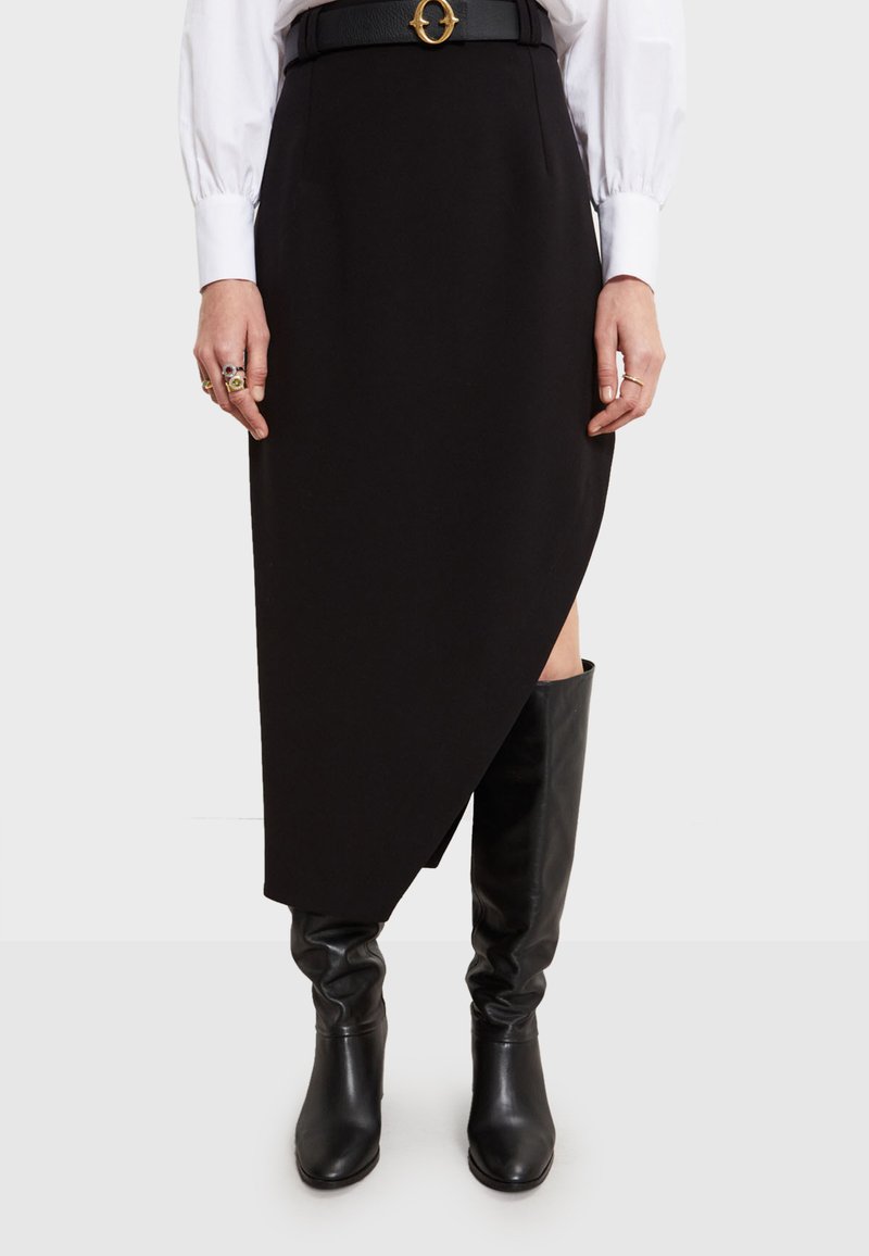 Crna suknja s asimetričnim rubom, izrađena od glatkog materijala, uparen s čizmama do koljena u crnoj boji i crnim remenom s okruglom kopčom.