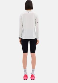 Light gray long-sleeve athletic shirt, black form-fitting shorts, pink running shoes, and gray striped socks. Simple design with logo accents.