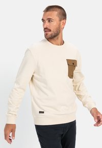 Crème sweatshirt met een bruine zak, ronde hals en ribgebreide manchetten. De zak heeft een klep en knoopsluiting. Etiket op de onderzoom.