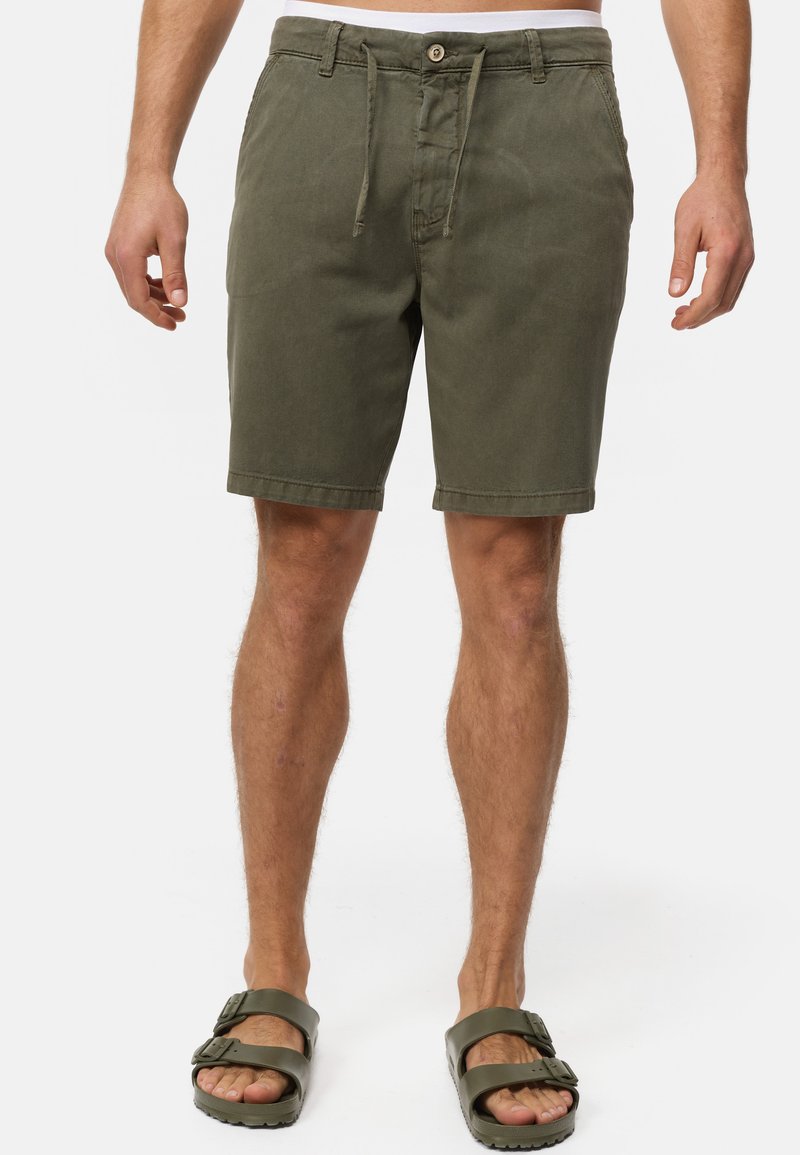 Khaki shorts with a drawstring and button closure, featuring two side pockets and rolled hems. Worn with dark green sandals.